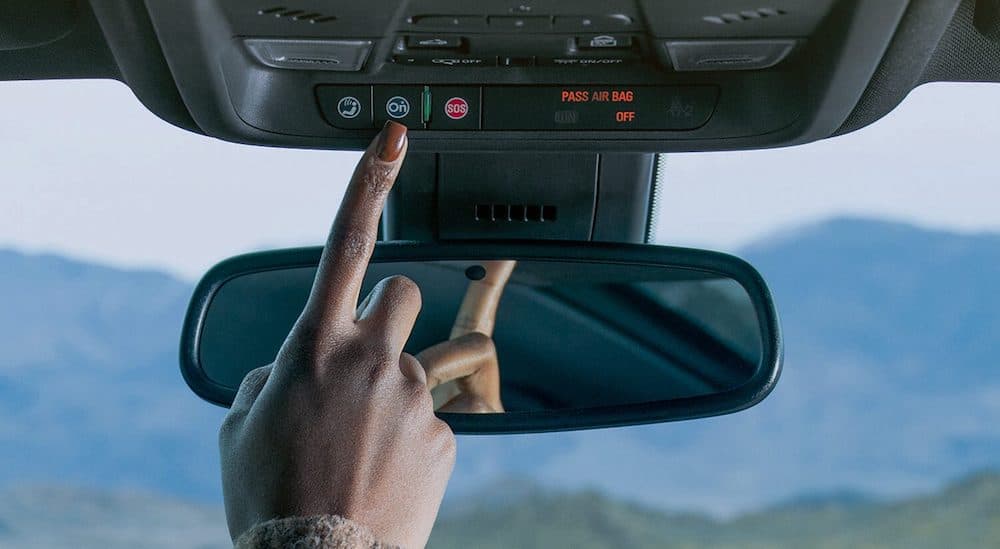 A hand is shown pressing an emergency call button in the interior of a car.