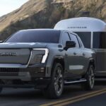 A grey 2024 GMC Sierra EV towing an Airstream trailer on a highway.