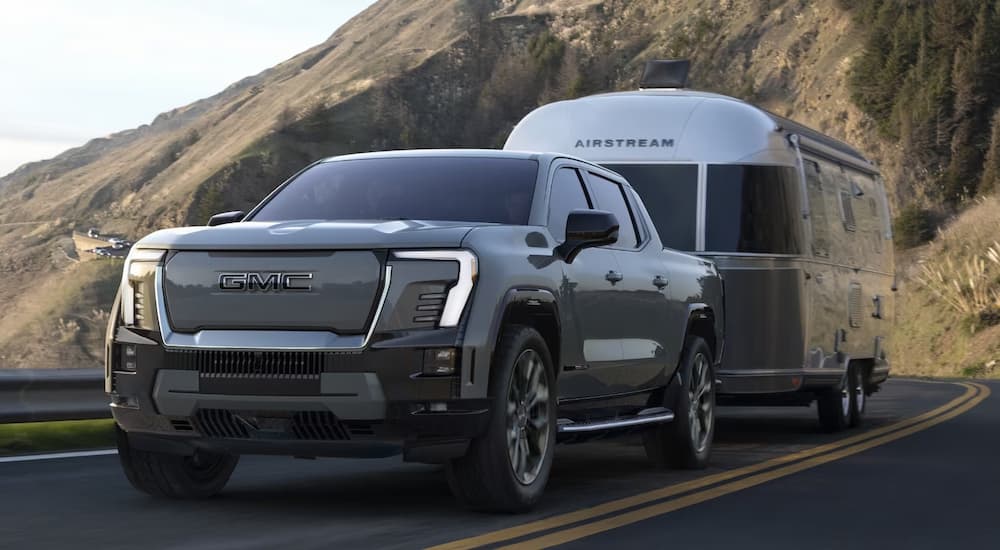 A grey 2024 GMC Sierra EV towing an Airstream trailer on a highway.