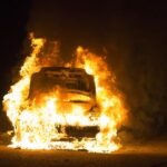 A car on fire, engulfed in flames at nighttime.