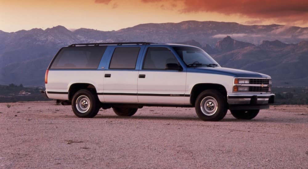 A white and blue 1992 Chevy Suburban is shown parked near mountains.