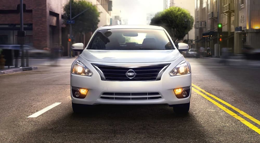 A white 2014 Nissan Altima is shown driving on a street after visiting a used car dealer.