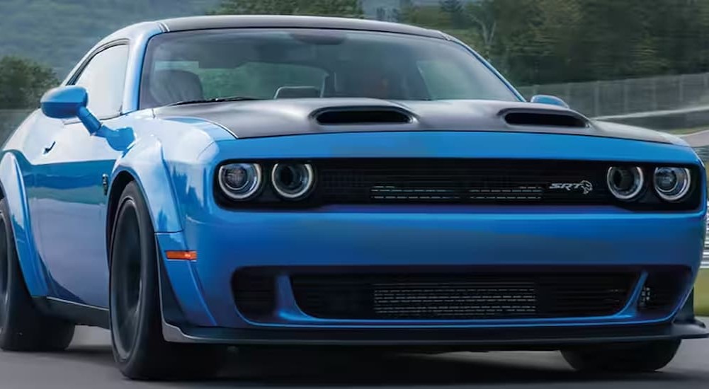 A blue 2023 Dodge Challenger SRT Hellcat is shown driving near a fence.