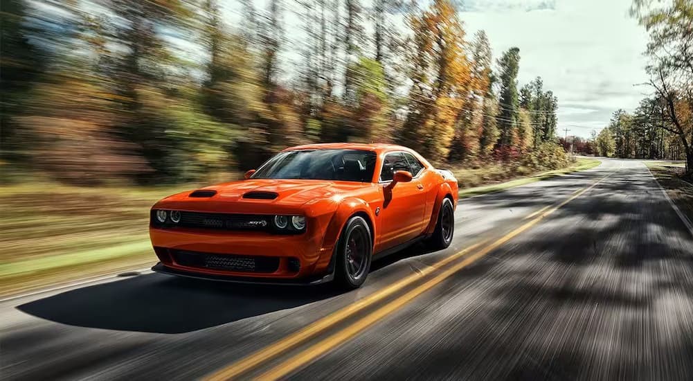 An orange 2023 Dodge Challenger SRT is shown driving on a highway after visiting a Used Dodge dealership.