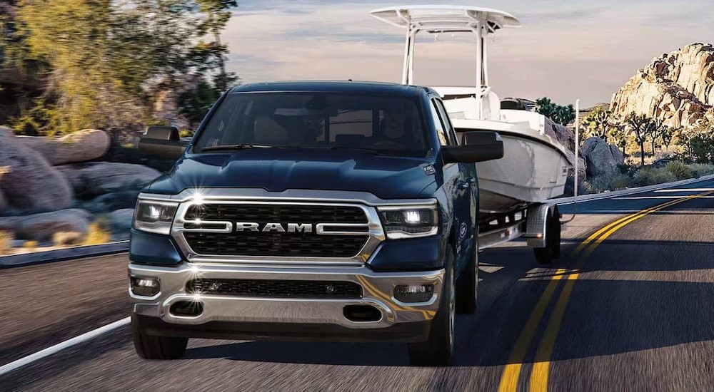A blue 2024 Ram 1500 for sale is shown towing a boat.