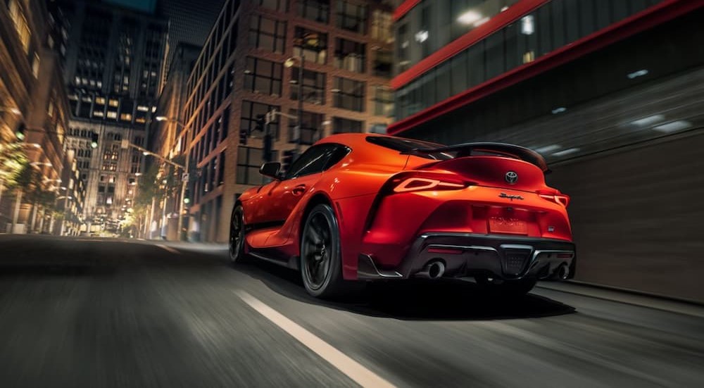 An orange 2024 Toyota GR Supra is shown driving on a city street.