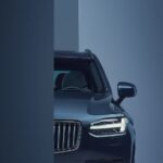 The drivers side of a blue 2024 Volvo CX90 with its signature headlight turned on.