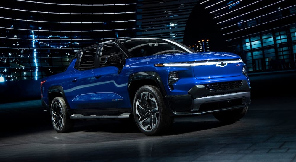 A preproduction image of a blue 2024 Chevy Silverado EV RST in dramatic lighting at a Chevy dealer.