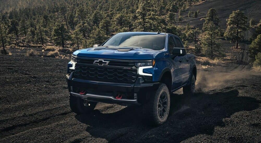 A blue 2024 Chevy Silverado 1500 for sale is shown driving off-road.