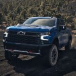 A blue 2024 Chevy Silverado 1500 ZR2 is shown driving off-road.