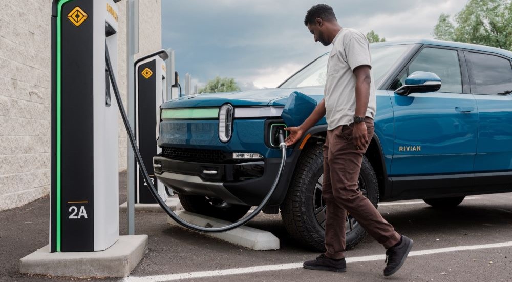 A person is shown plugging in a blue 2023 Rivian R1T. 