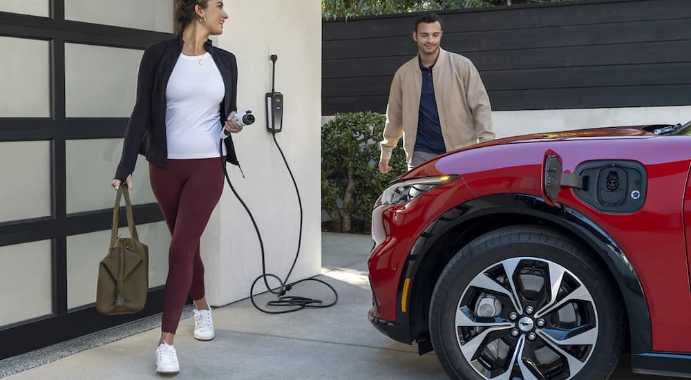 Two people are shown walking past a red 2023 Ford Mustang Mach-E charging in a garage.