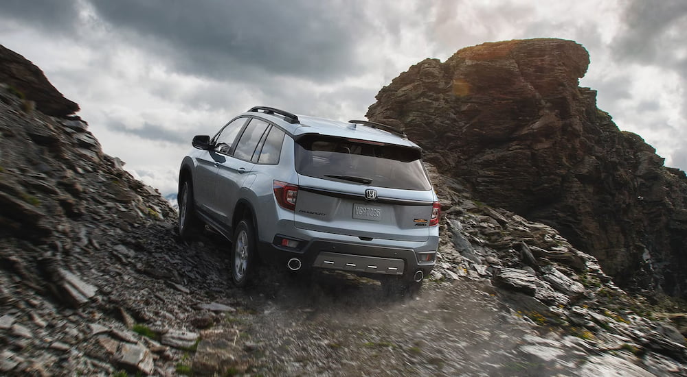 A grey 2024 Honda Passport TrailSport is shown from the rear driving up a steep hill after leaving a Honda dealer.