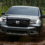 A grey 2024 Honda Ridgeline TrailSport is shown off-roading on a muddy path.