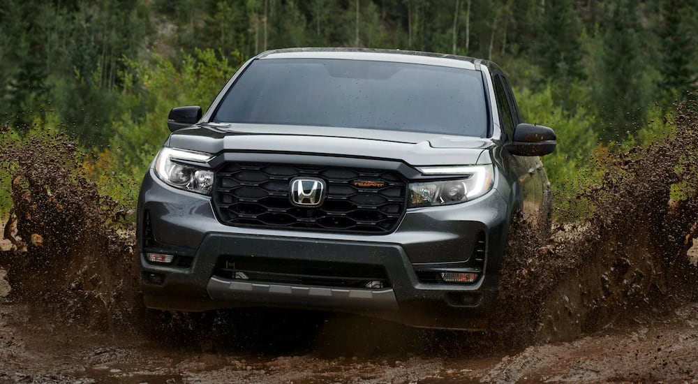 A grey 2024 Honda Ridgeline TrailSport is shown off-roading on a muddy path.