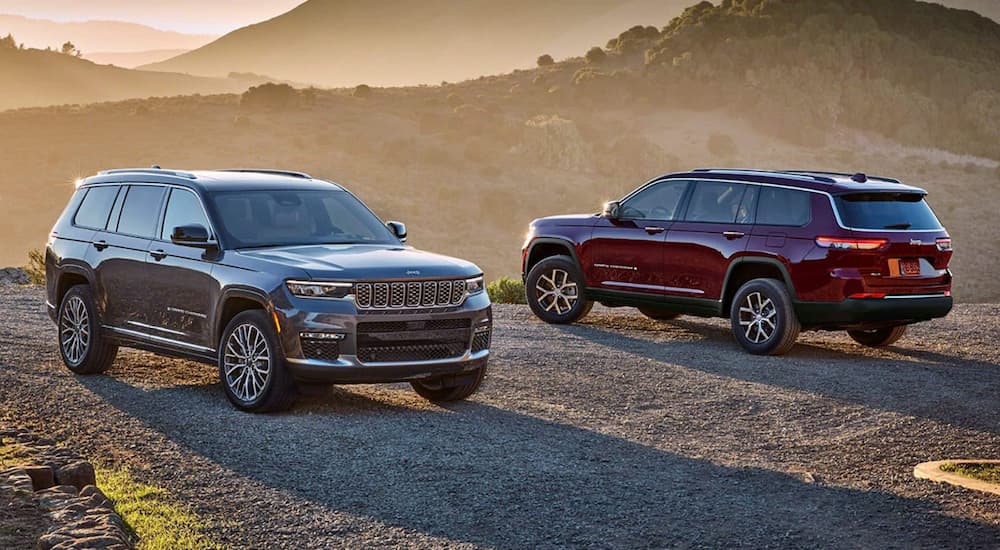 A grey 2024 Jeep Grand Cherokee Summit and a red 2024 Jeep Grand Cherokee Limited parked in a clearing at sunset.