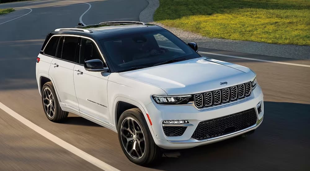 A white 2024 Jeep Grand Cherokee for sale driving on an open road.