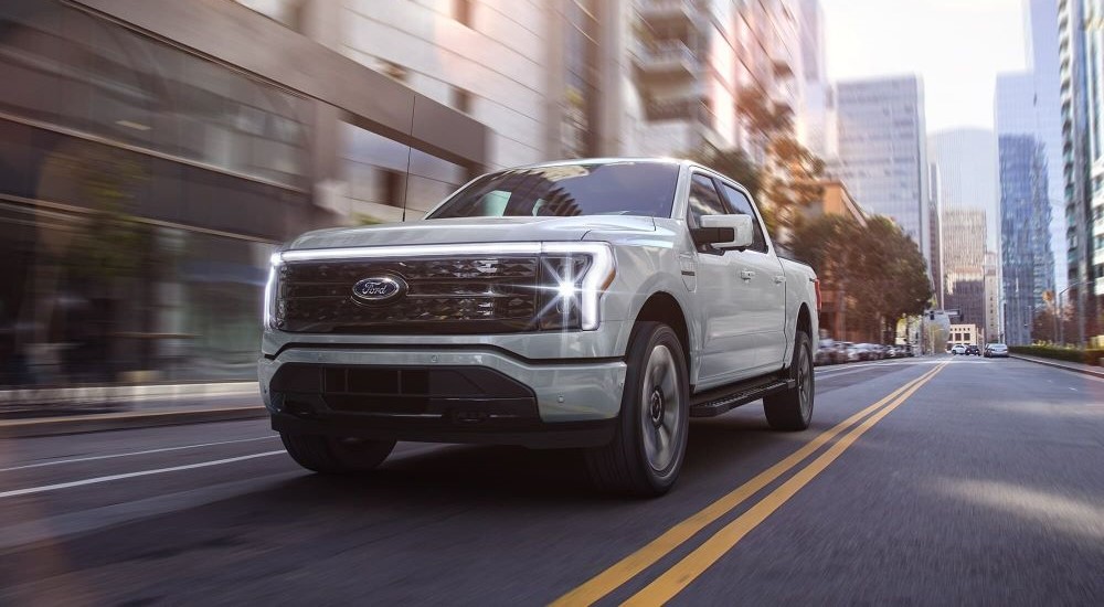A white 2023 Ford F-150 Lightning is shown driving in a city.
