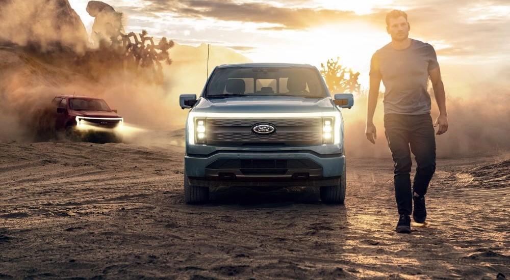 A blue 2023 Ford F-150 Lightning is shown from a front angle while parked off-road.
