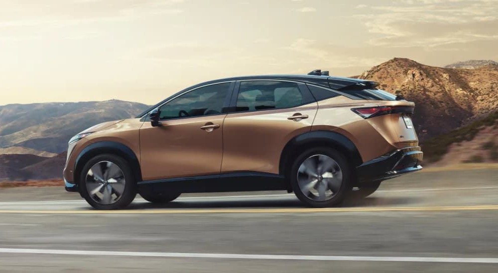 A side view of an orange 2024 Nissan ARIYA driving.
