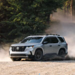 A silver 2025 Honda Pilot TrailSport driving on a dirt trail.