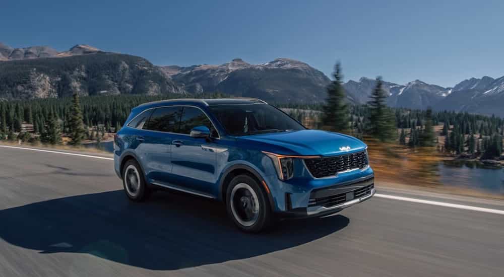 A blue 2025 Kia Sorento Hybrid driving on an open road through the mountains.