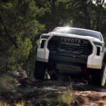 A white 2024 Toyota Tundra TRD Pro driving through a forest.