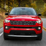 Head-on view of a red 2024 Jeep Compass driving on an open road.
