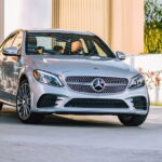 A white 2020 Mercedes-Benz C-Class driving by a building.