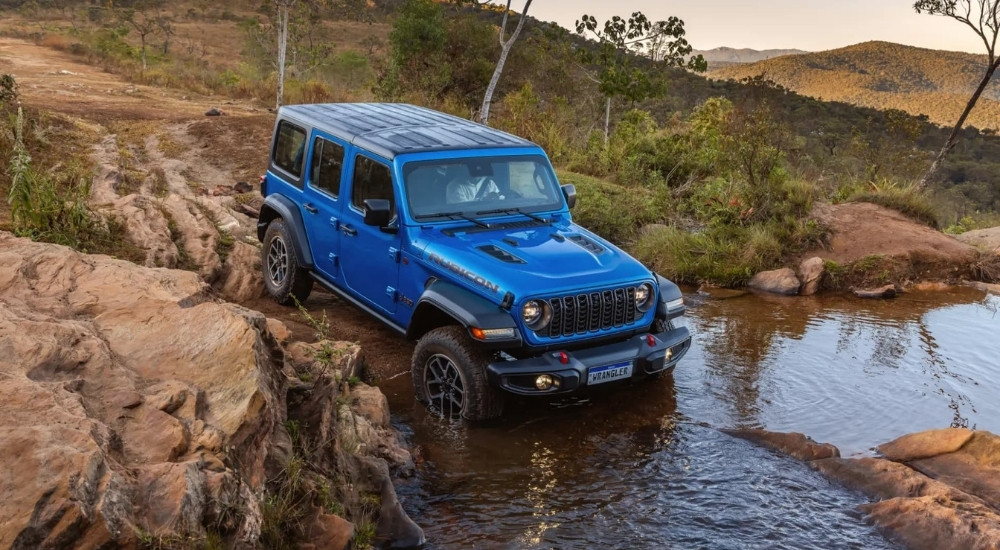 A blue 2025 Jeep Wrangler Unlimited Rubicon is shown driving through water.