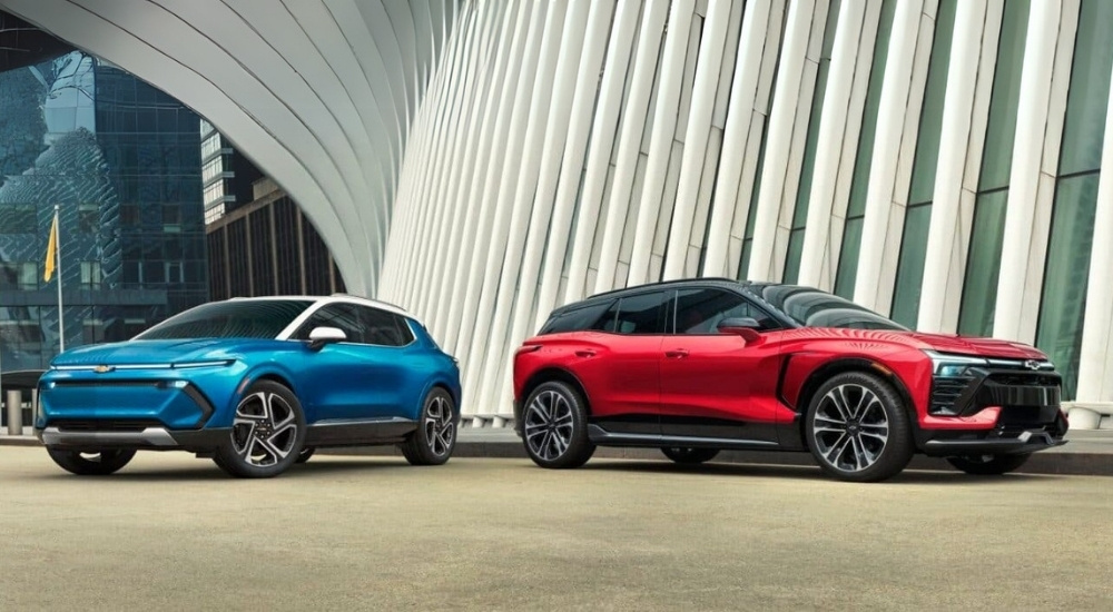 A blue 2024 Chevy Equinox EV and a red Blazer EV are shown near a modern building.