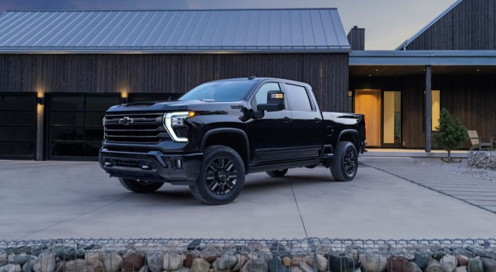 The black 2024 Chevy Silverado 2500 HD High Country is shown parked near a house.