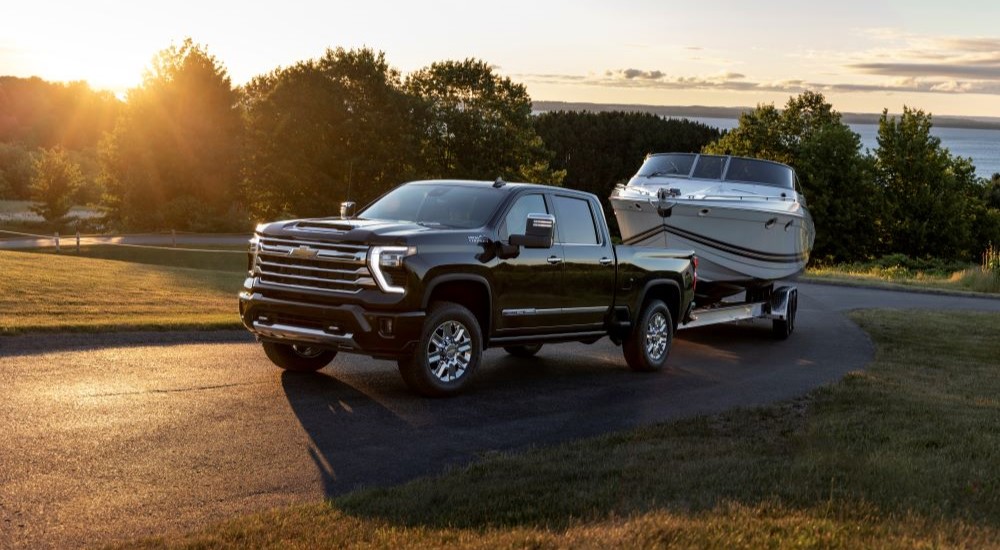 A black 2024 Chevy Silverado 2500 HD High Country is shown towing a boat.