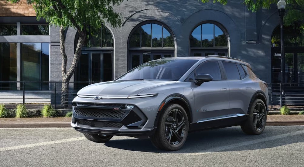 A silver 2025 Chevy Equinox EV RS is shown parked near a building.