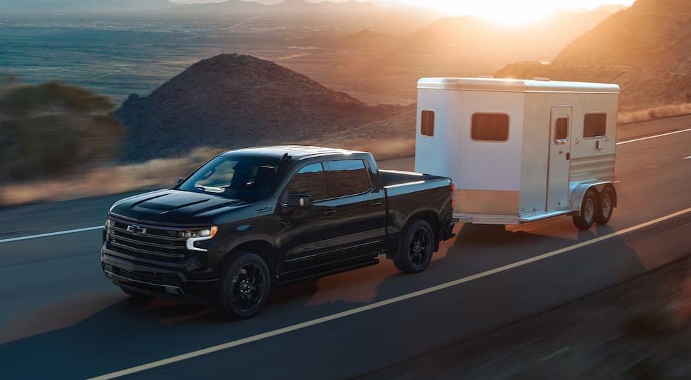 A black 2025 Chevy Silverado 1500 High Country is shown towing a trailer.