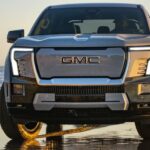 A silver 2025 GMC Sierra EV Denali is driving on a beach.