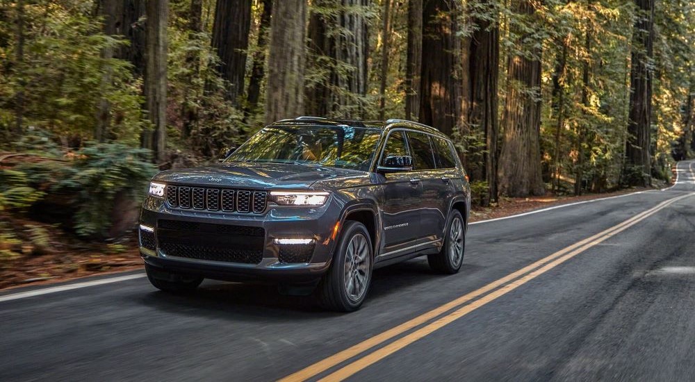 A grey 2021 Jeep Grand Cherokee L driving through a forest.