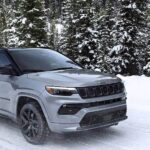 A grey 2025 Jeep Compass Trailhawk driving down a snowy road.