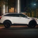 Side of a white 2025 Kia Sorento driving on a city street.