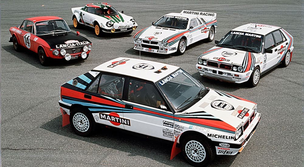 Five different years of Lancia "Rally Queens" are shown parked on pavement.