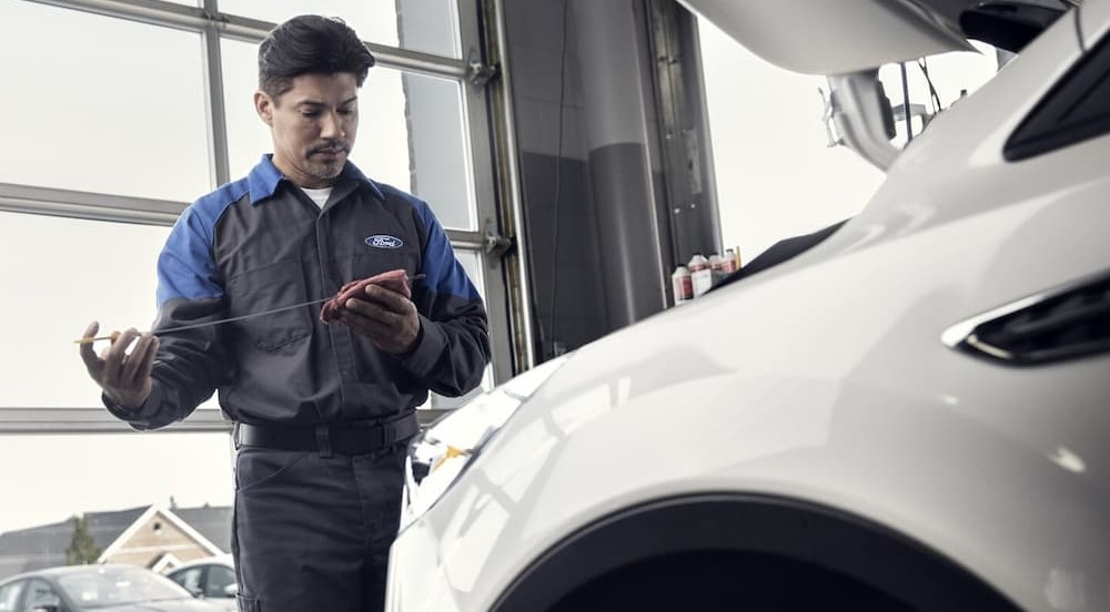 A mechanic is shown checking the oil on a white vehicle.