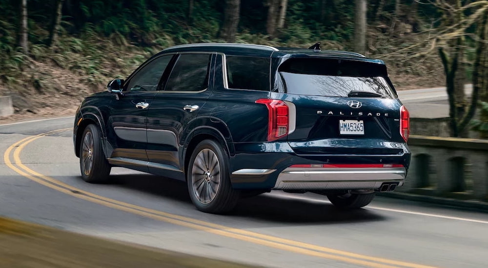 Rear of a blue 2024 Hyundai Palisade driving around a bend.