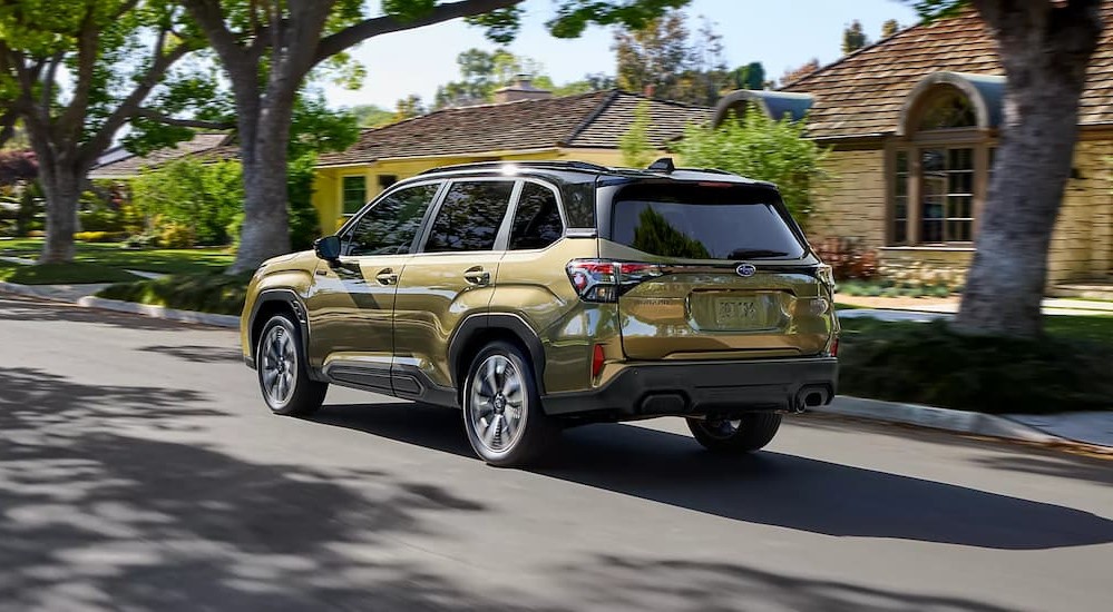 A green 2025 Subaru Forester Hybrid driving near a house.