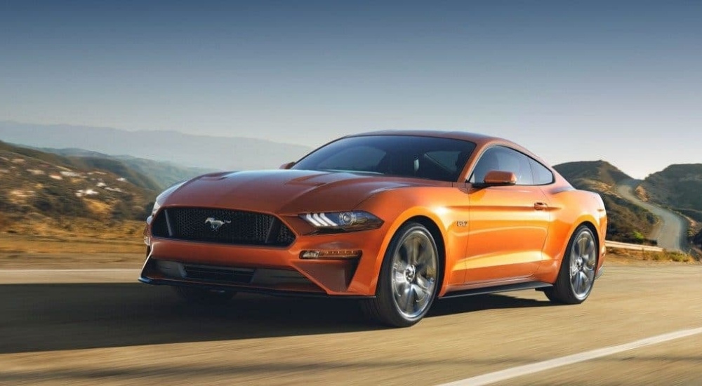 An orange 2017 used Ford Mustang GT for sale driving on an open road.