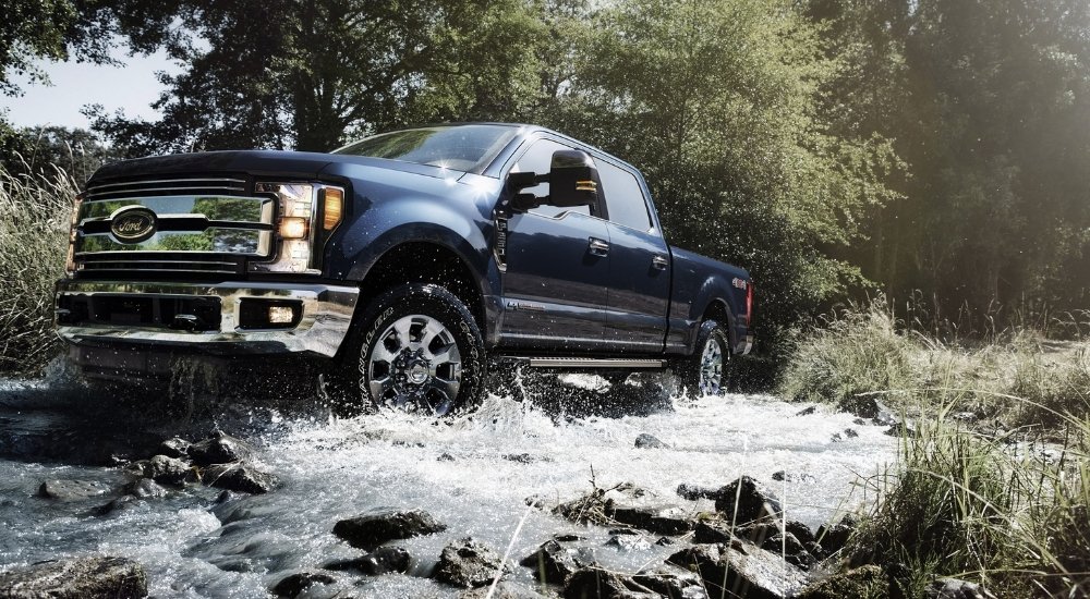A blue 2019 Ford F-250 splashing through a creek.