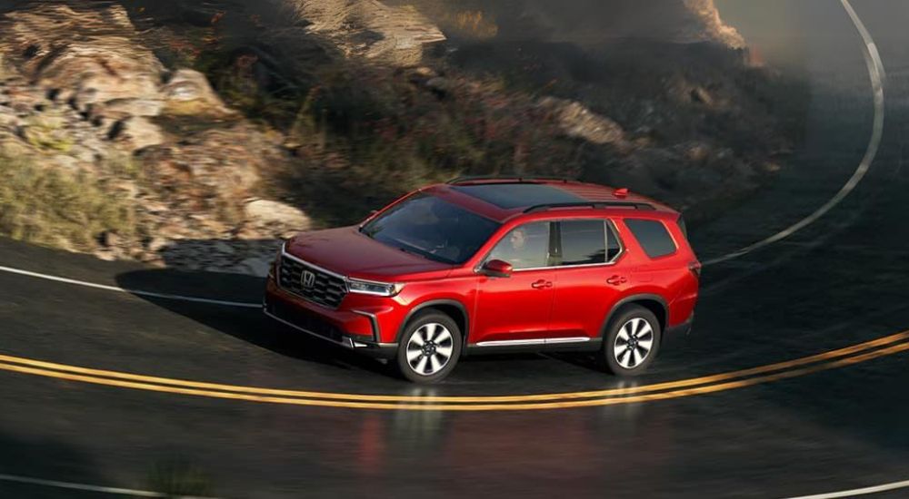 A red 2025 Honda Pilot taking a corner on a highway
