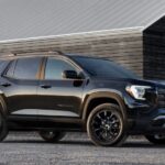 A black 2025 GMC Terrain parked near a wooden house.