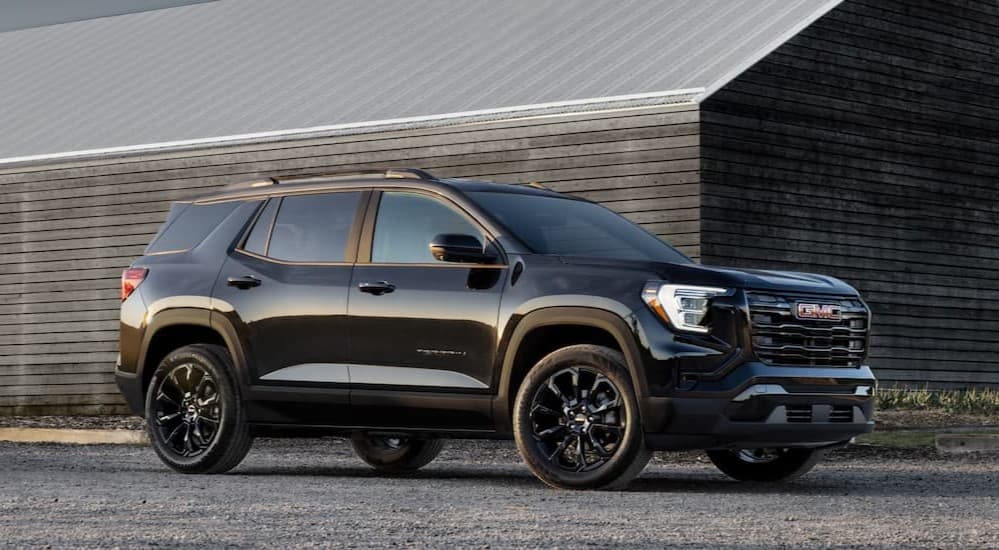 A black 2025 GMC Terrain parked near a wooden house.