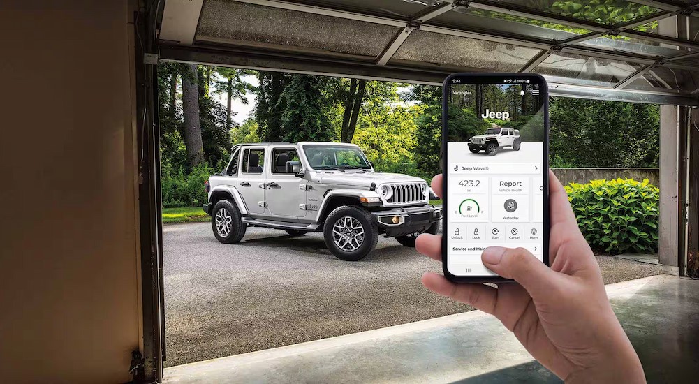 A person using the Jeep app on a cellphone near a white 2024 Jeep Wrangler.