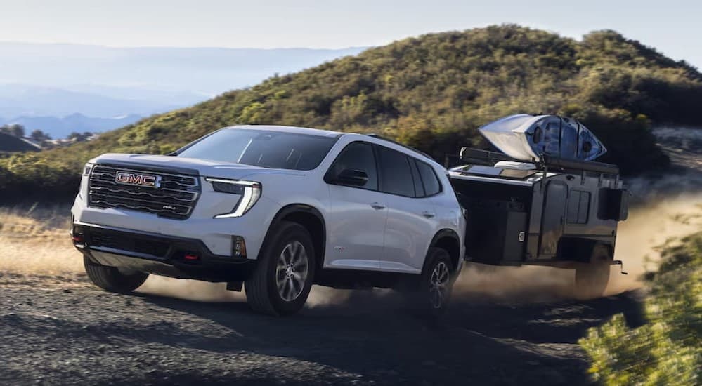 A white 2025 GMC Acadia AT4 towing a trailer on a dirt road.